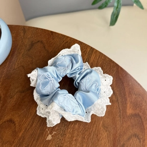 Dettaglio di un elastico in raso azzurro con bordo in pizzo bianco su sfondo di legno