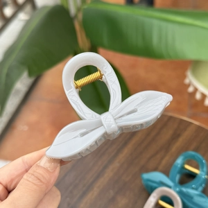 Close-up of marble pattern bow hair claw clip with golden metal spring held by hand