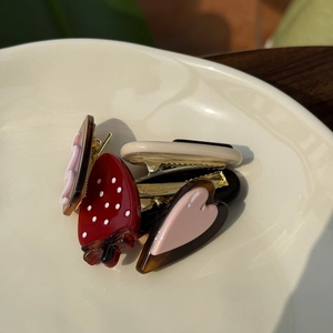 Détail de barrettes en acétate en forme de fruit et cœur avec strass sur un plat blanc