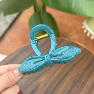 Close-up of a teal bow-shaped hair claw clip with a shiny finish and gold spring