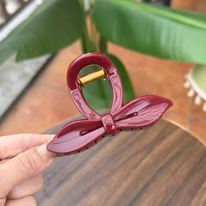 Close-up of a burgundy wine red bow hair claw clip with a glossy finish and gold spring