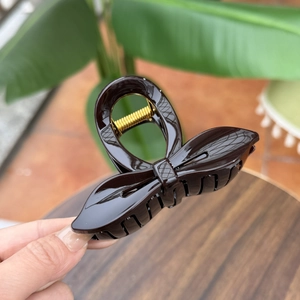 Detailed view of the dark brown bow-shaped hair claw with glossy finish and gold metal spring