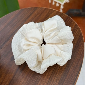 Elegant cream pleated chiffon scrunchie with a silky satin finish on a wooden stand