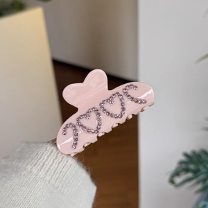 Pink acetate heart hair claw with LOVE rhinestone crystals shown in a hand