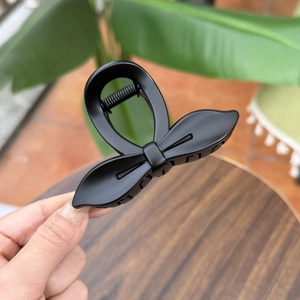 Detail of matte black bow hair claw clip showing textured finish and spring mechanism