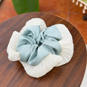 Detail of white pleated fabric and mint green silk-like scrunchie on a wood stand