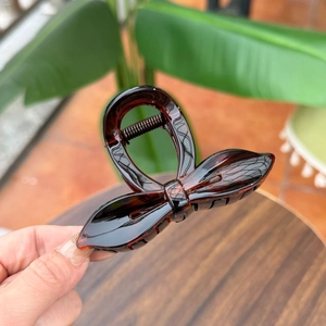 Macro view of translucent amber bow hair claw clip with glossy resin finish and metal spring