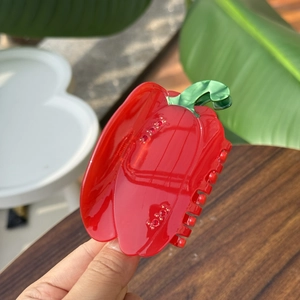 Détail d'une pince à cheveux piment rouge avec tige verte et strass brillants