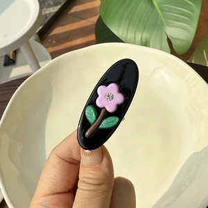 Gros plan sur la pince à cheveux ovale noire avec fleur en strass rose et feuilles vertes