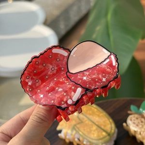 Détail d'une pince à cheveux en acétate en forme de litchi tenue à la main au soleil