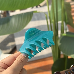 Detail of a glossy teal butterfly hair claw clip being held outdoors for size reference