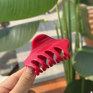 Close-up of vibrant red plastic hair claw with curved teeth held in natural sunlight