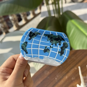 Blue acetate ocean earth hair claw clip with world map pattern held in hand outdoors