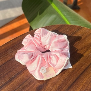 Chouchou en satin rose avec bouton fleuri et lumière douce sur surface en bois