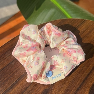 Chouchou en satin à fleurs avec bouton et liseré rose sur une surface en bois