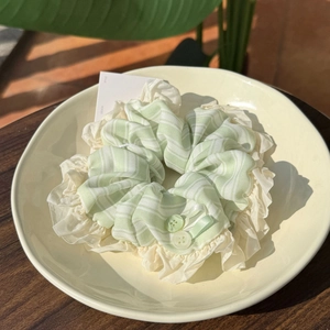 Frisches gestreiftes Scrunchie mit Rüschen und grünen Knöpfen auf Cremeteller
