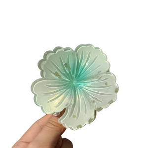 Translucent light green flower hair claw clip with golden glitter in hand-held display