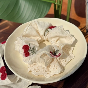 Beige cherry embroidered scrunchie with lace trim on a leaf and wooden background