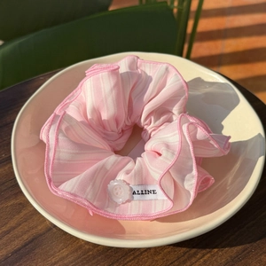 Pink and white striped scrunchie with button detail and woven label on ceramic tray