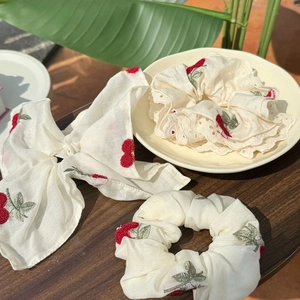 Detailed embroidery of red cherries on cream lace and silk hair accessories