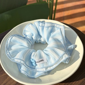 Detail of blue striped scrunchie with floral button and ALLINE label on white plate