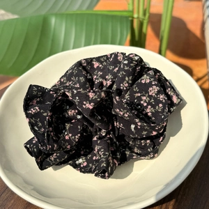 French floral hair scrunchie with pink blossoms on black fabric in a ceramic dish