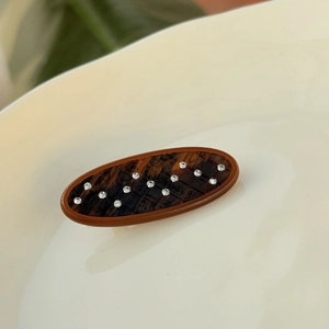 Détail d'une pince à cheveux ovale marron avec motif losanges et strass en forme de vague