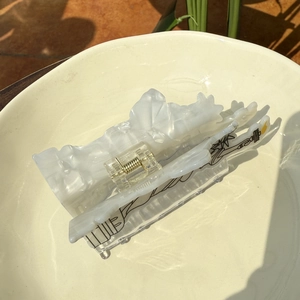 White acetate hair claw clip with Statue of Liberty line art on a ceramic plate