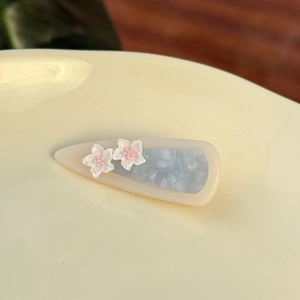 Detail of teardrop acetate hair clip with blue marble texture and white 3D flowers