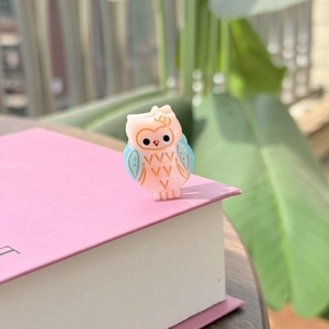 Vue détaillée d'une pince à cheveux hibou en acétate rose et bleu sur un livre