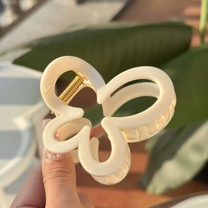 Détail d'une pince à cheveux fleur blanc cassé tenue sur un fond de feuillage naturel