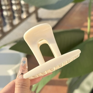 Gros plan d'une pince à cheveux minimaliste crème tenue à la lumière naturelle du soleil