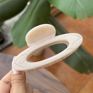 Detail of a 10cm cream beige marbled hollow hair claw clip held over a wooden table