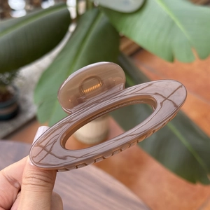 Close-up of a brown marble acrylic hair claw clip held against a natural green leaf background