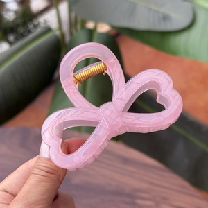 Close-up of translucent pink heart hair claw clip with golden metal spring detail