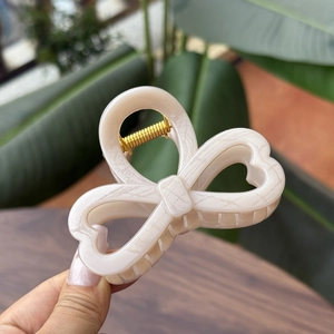 Detailed close-up of cream bow hair claw clip showing strong gold metal spring mechanism