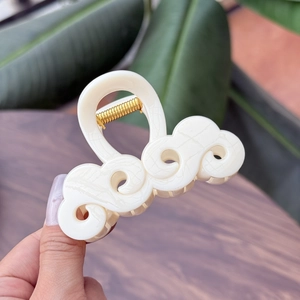Vista macro di un fermaglio per capelli in acetato bianco panna con design a onde e ritagli