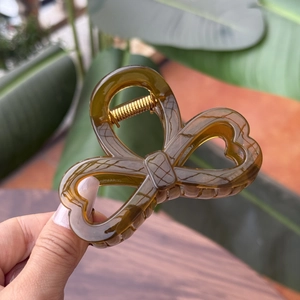 Detailed close-up of amber brown bow hair claw clip with golden metal spring mechanism