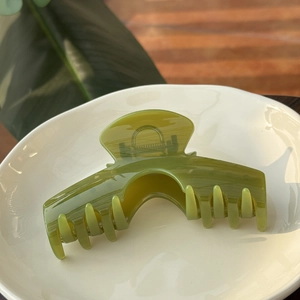 Pince à cheveux arquée translucide vert olive pour cheveux épais sur plat en céramique