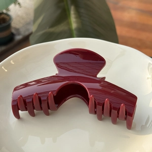 Grosse pince à cheveux rouge foncé brillante sur assiette blanche avec décor de feuille