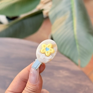 Bloem haarclip van acetaat met gele bloem en blauw hart op marmerwit voetstuk