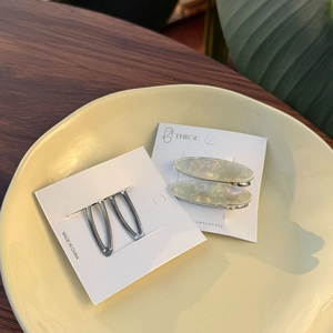 Detailed view of acetate oval hair clips and silver metal pins on white retail cards