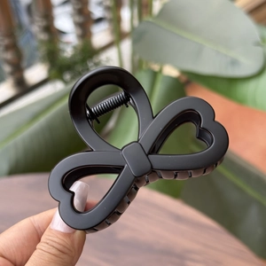 Detail of matte black heart-shaped hair claw clip with bow-knot design and metal spring