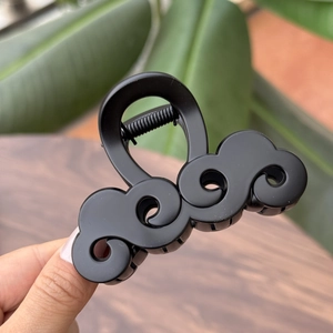 Dettaglio della pinza per capelli nera opaca con elegante design a nuvola e molla in metallo