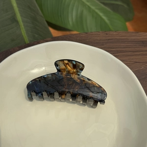 Classic amber acetate hair claw clip with tortoiseshell pattern on white ceramic plate