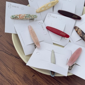 Close-up of elegant acetate oval duckbill hair clips in various colors on a ceramic plate