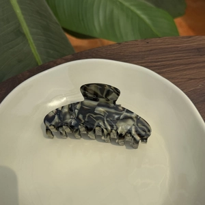 Elegant marbled acetate hair claw clip with seven teeth on a ceramic tray display