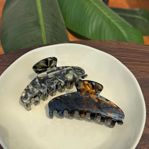 Detail of marble and tortoiseshell acetate hair claws on a tray with green leaves