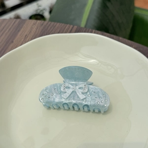 Elegant light blue bow claw clip with sparkling rhinestones on a ceramic display plate