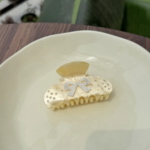 Elegant cream bow hair claw clip with rhinestones shown on a decorative ceramic plate